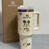 Gourde Stanley Flowstate Tumbler 40 oz / 1.19 L avec anse — crème/beige avec motifs foncés et bande métallique irisée, motif personnage rond assis à grande tête et