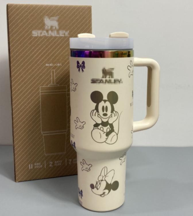 Gourde Stanley Flowstate Tumbler 40 oz / 1.19 L avec anse — crème/beige avec motifs foncés et bande métallique irisée, motif personnage rond assis à grande tête et