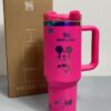 Gourde Stanley Flowstate Tumbler 40 oz avec anse — rose fuchsia avec motifs sombres et bande métallique irisée, motif personnage rond assis à grande tête et