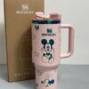 Gourde Stanley Flowstate Tumbler 40 oz avec anse — rose pâle avec motifs bleu-vert et bande métallique irisée, motif personnage rond assis à grande tête et