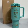 Gourde Stanley Flowstate Tumbler 40 oz avec anse — turquoise avec motifs dorés, motif personnage rond assis à grande tête et