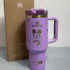 Gourde Stanley Flowstate Tumbler 40 oz avec anse — violet/lilas avec motifs dorés, motif personnage rond assis à grande tête et